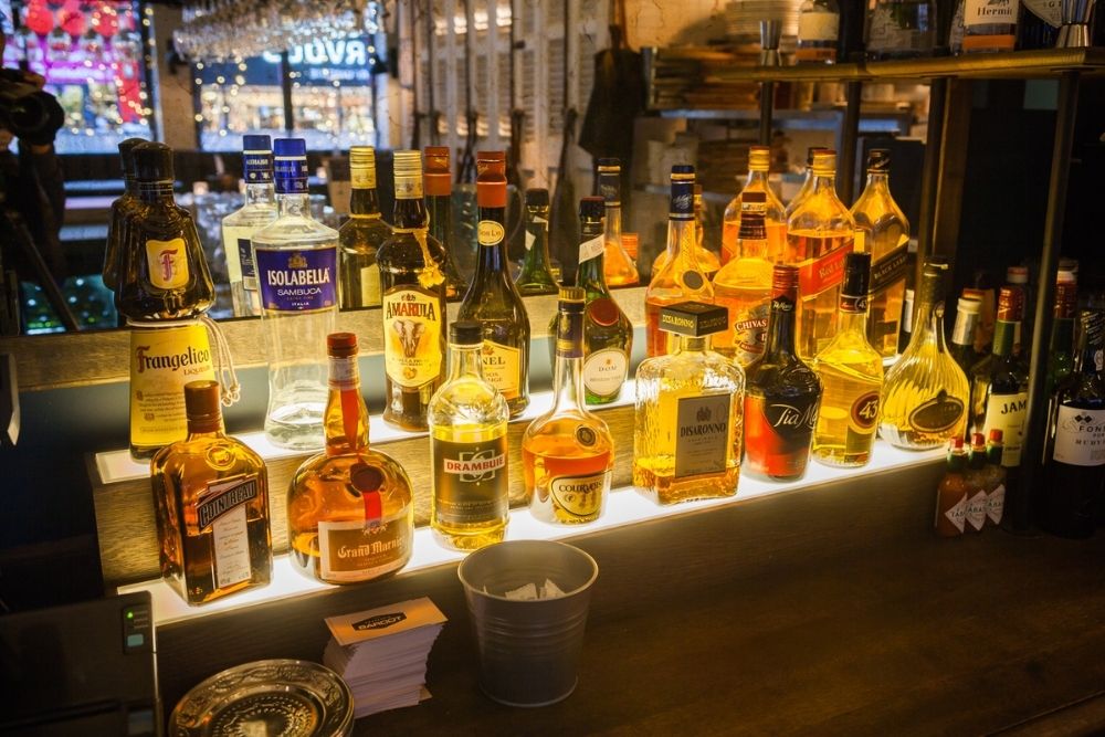 Een bar met verschillende flessen drank die naast elkaar op een verlicht plankje staan