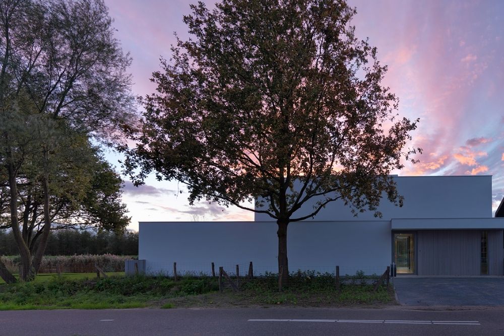 Een strakke witte woning aan de straat met een boom op de voorgrond tijdens zonsondergang