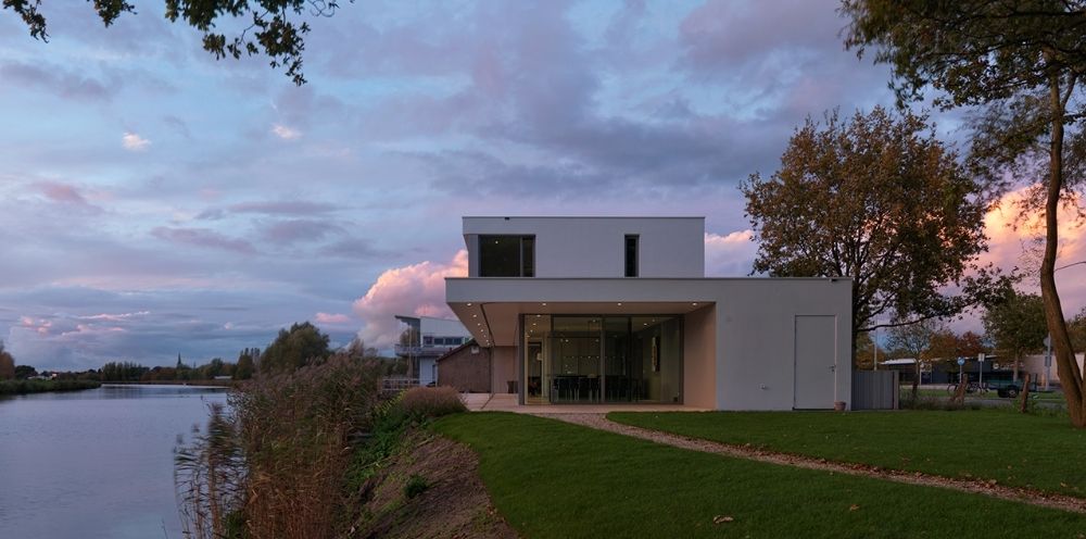 Een strakke woning met grote ramen naast een rustige rivier in de avondlucht