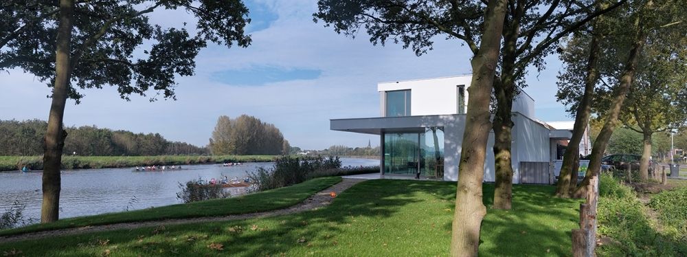 Modern huis aan een rustige rivier omringd door groene bomen en een ruim grasveld