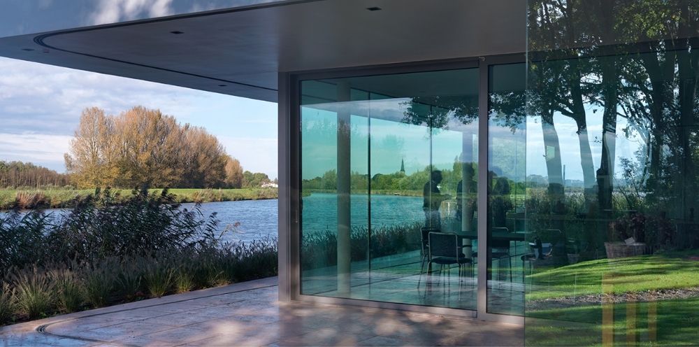 Moderne glazen pui met zicht op water bomen en een groene tuin