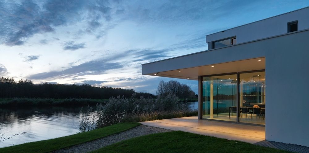 Moderne woning aan het water tijdens de schemering met grote ramen en uitzicht op een rustige plas