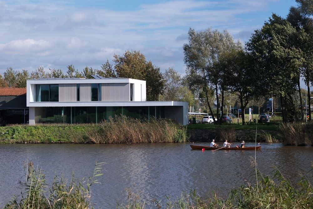 Strakke witte woning langs een rustige rivier met een kleine boot op de voorgrond
